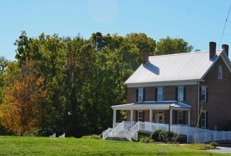 Brick house with white porch and green trees.
